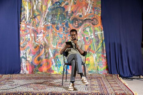 Poet reading from a tablet in front of a painted backdrop