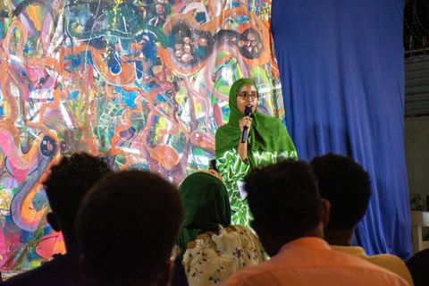 Poet performing in front of a painted backdrop at the open mic