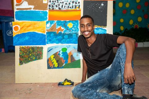 Artist beside the wall of paintings from the art therapy workshop